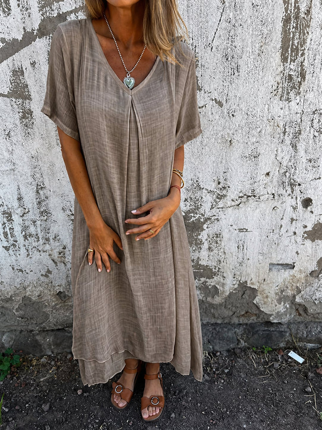 Model wearing a loose flowy V-neck dress in beige, standing in a relaxed casual pose