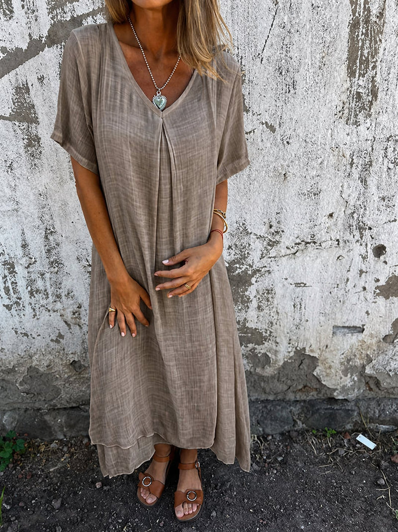 Model wearing a loose flowy V-neck dress in beige, standing in a relaxed casual pose