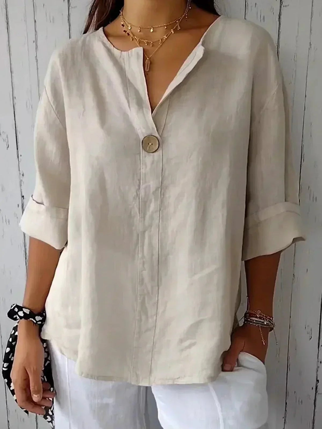 Model wearing a relaxed casual V-neck blouse with a single-button detail in a neutral beige color