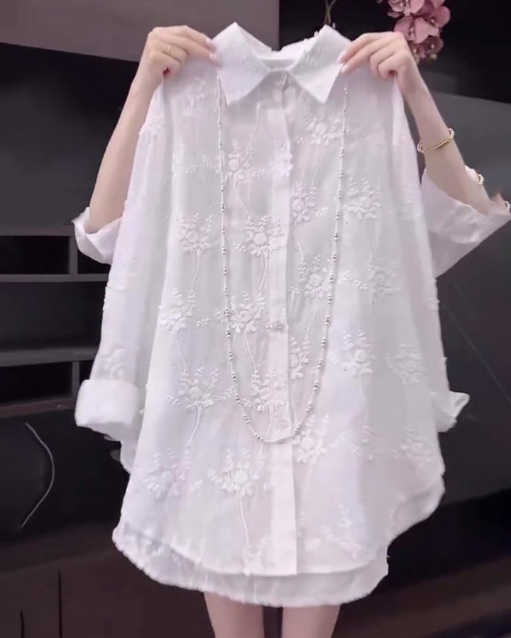 Woman wearing a white loose-fit floral embroidered dropped-shoulder shirt, front view