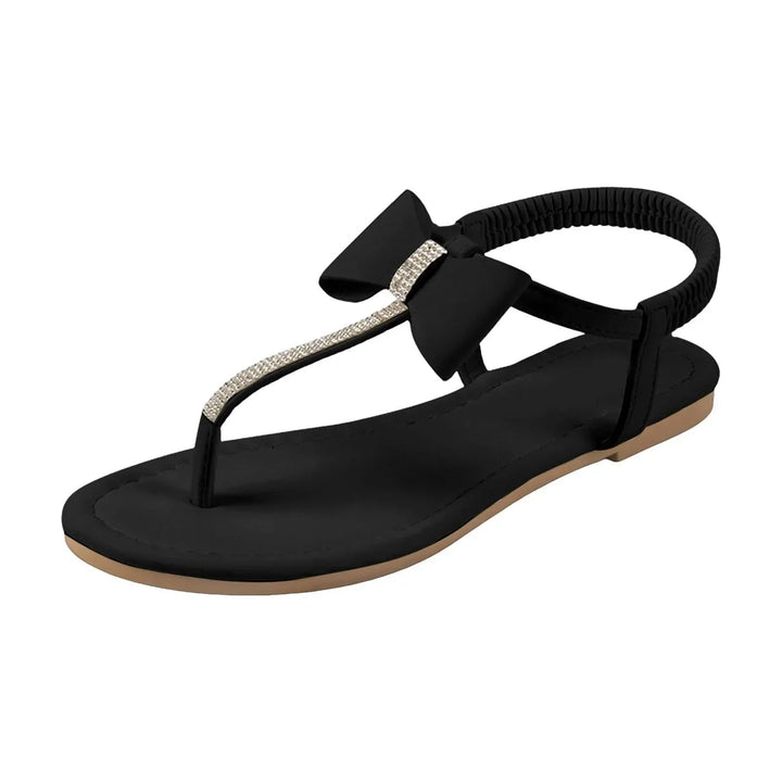 Close-up of rhinestone embellishment and bow accent on Antoinette flat sandals in black