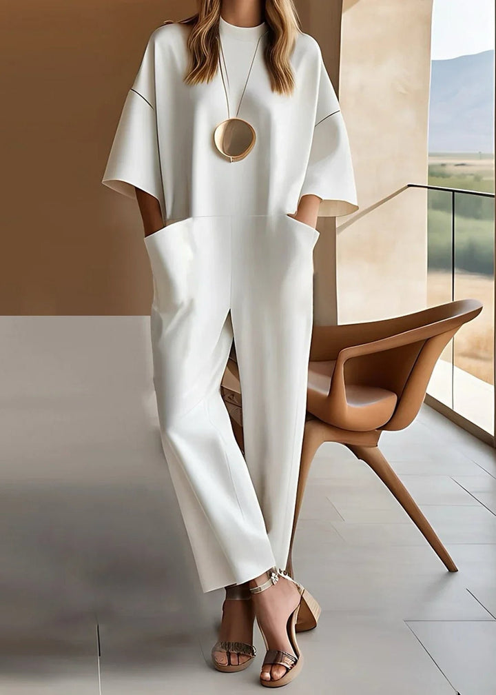 Woman wearing a white wide leg jumpsuit with drop-shoulder short sleeves and a crew neckline, styled with heeled sandals