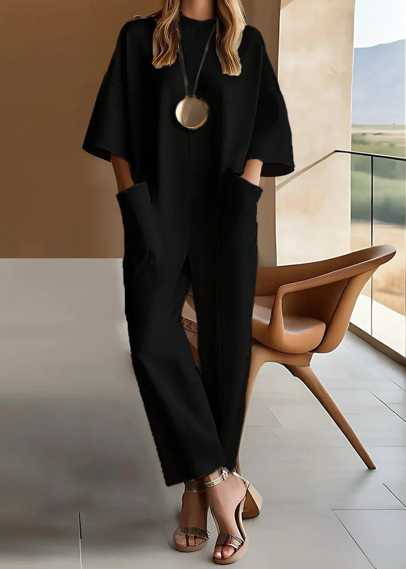 Back view of a black wide leg jumpsuit with short sleeves and deep side pockets, showing the full-length straight-leg silhouette