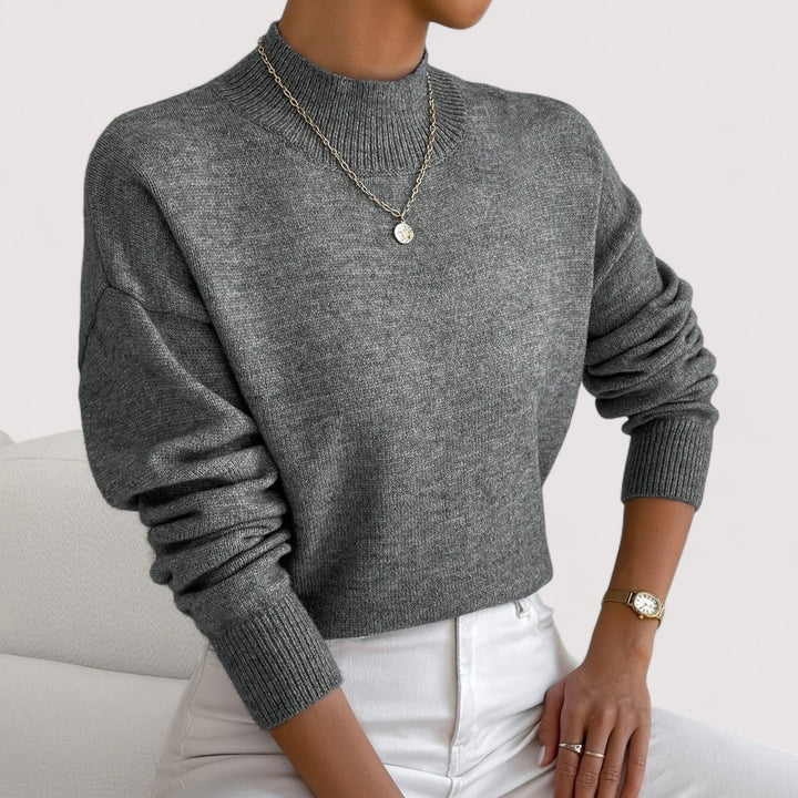 Model wearing a pink turtleneck sweater in a cozy home setting