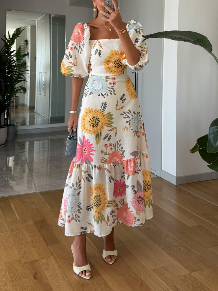 Woman wearing a multicolor floral midi dress with a square neckline, puff sleeves, and a layered ruffled hem