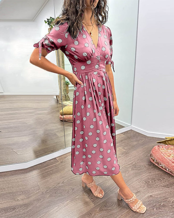 Woman smiling in a green polka dot dress at an outdoor garden setting