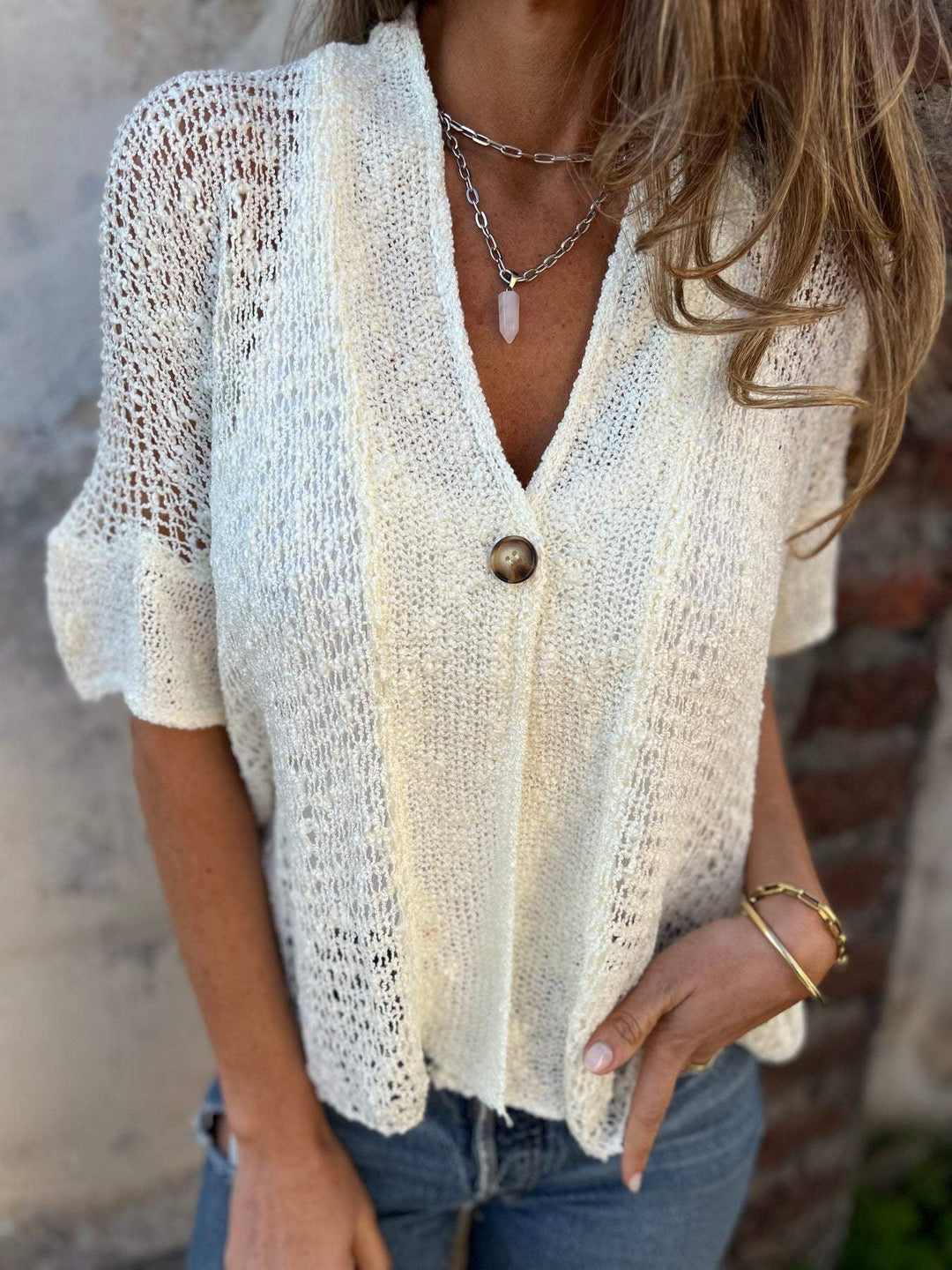 Close-up of the decorative button accent at the V-neckline on the white textured knit top