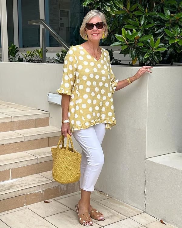 Woman wearing a sky blue polka dot V-neck blouse with a relaxed fit, smiling confidently