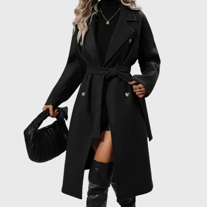 Woman wearing a black longline winter trench coat with adjustable belt and buttoned cuffs, front view