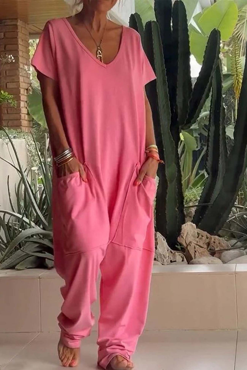 Woman wearing a loose pink V-neck short sleeve jumpsuit with oversized front pockets and drop-crotch relaxed leg