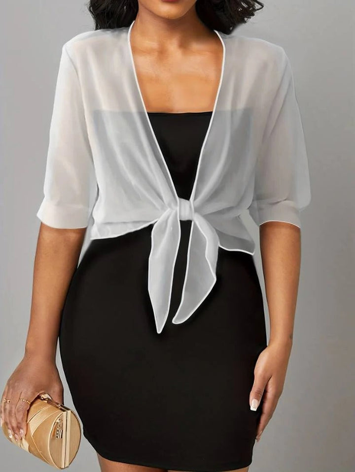 Woman wearing a white sheer tie front blouse with 3/4 roll-tab sleeves and a knotted hem