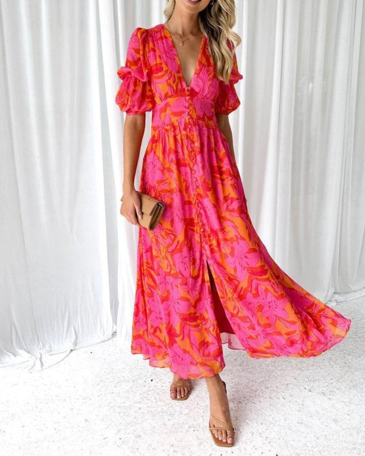 Woman wearing a flowing red-pink maxi dress with delicate puff sleeves, standing in a sunlit outdoor setting
