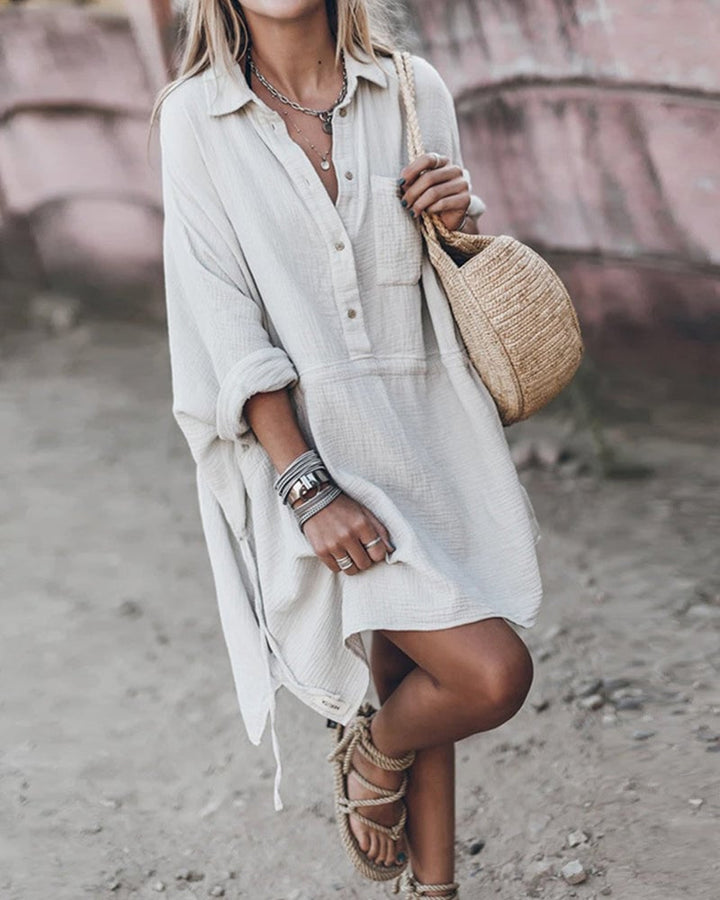 Woman wearing a white collared flowy shirt dress with a softly defined waist and flowing skirt