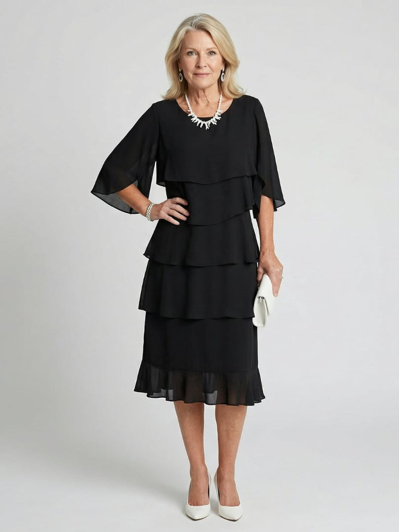 Woman wearing a black tiered flutter sleeve midi dress with a round neckline, flowing layered skirt falls between knee and ankle