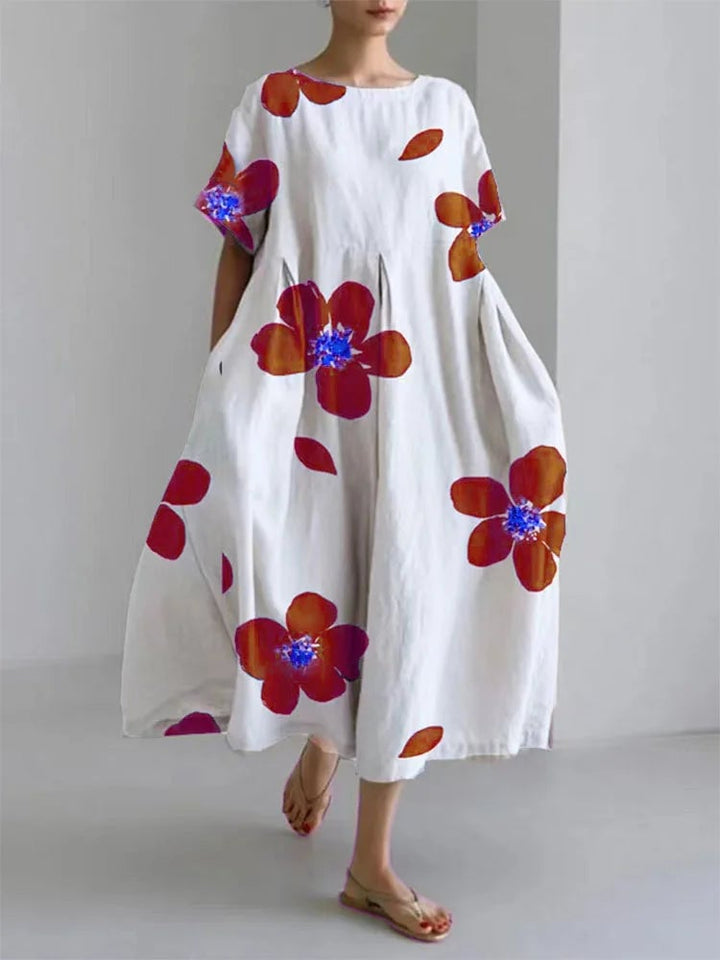 Woman wearing the Caterina long floral dress in red with vibrant flower print and flowing pleated silhouette
