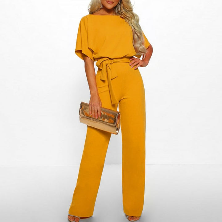Woman wearing a yellow belted wide-leg batwing jumpsuit with floor-grazing trousers and a self-tie waist belt