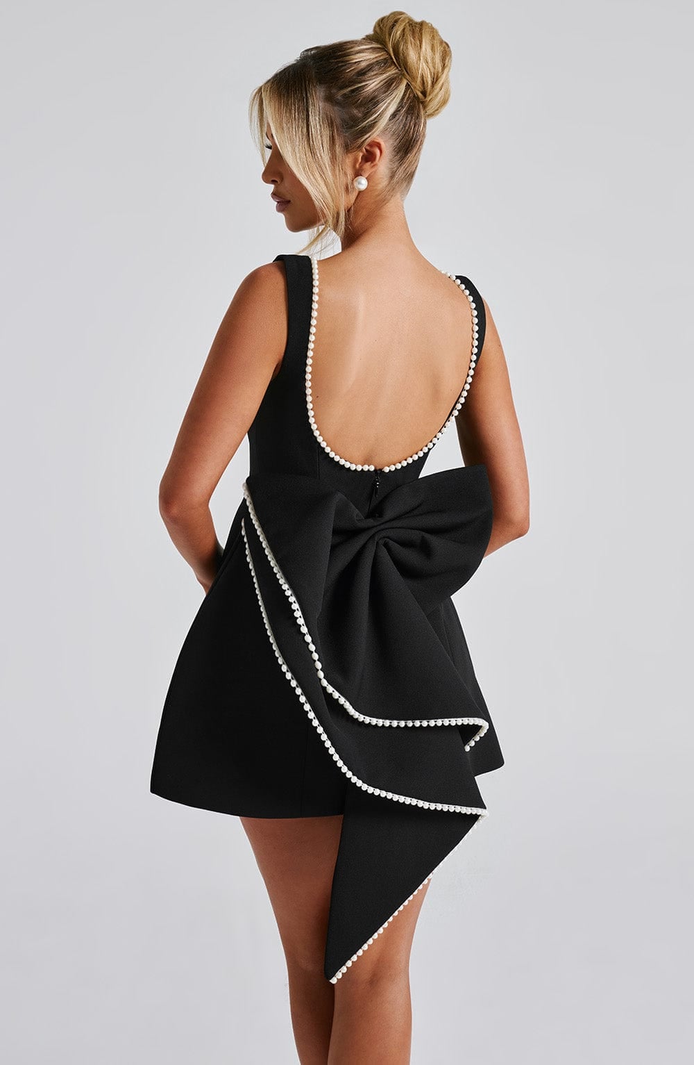 Close-up of the pearl bow accent on the back of the Celeste mini dress in black