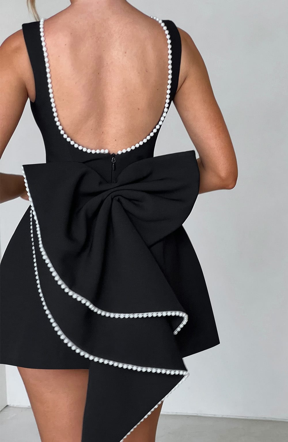 Back view of Celeste mini dress in white showing the pearl-edged bow and sleeveless cut