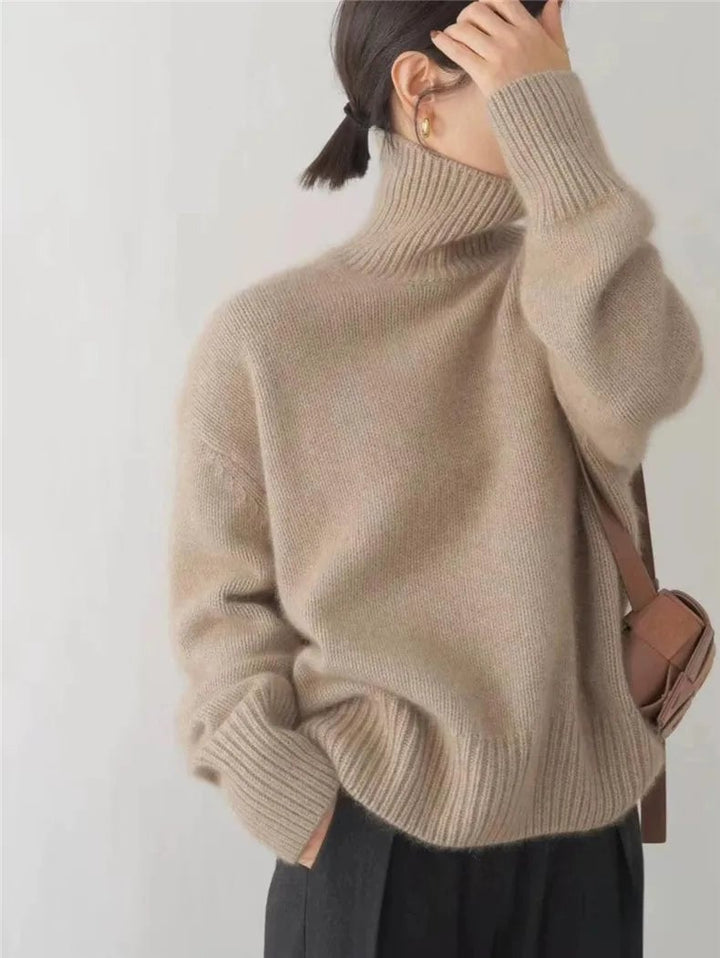 Full-length shot of a woman wearing a khaki high collar sweater paired with jeans and ankle boots