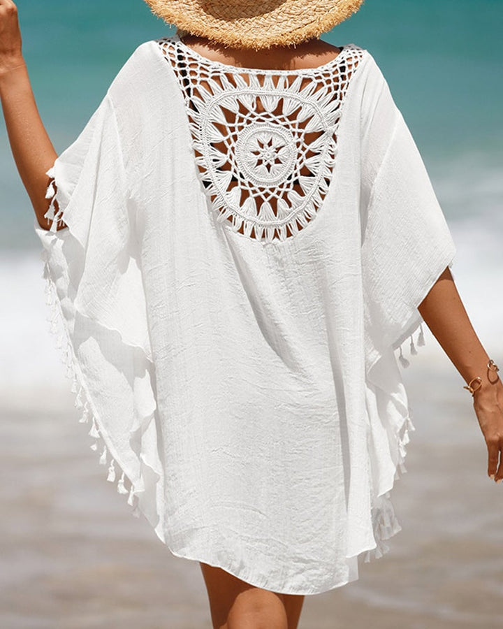 Woman wearing a white boho beach cover-up with crochet-inspired pattern and tassel hem at the beach