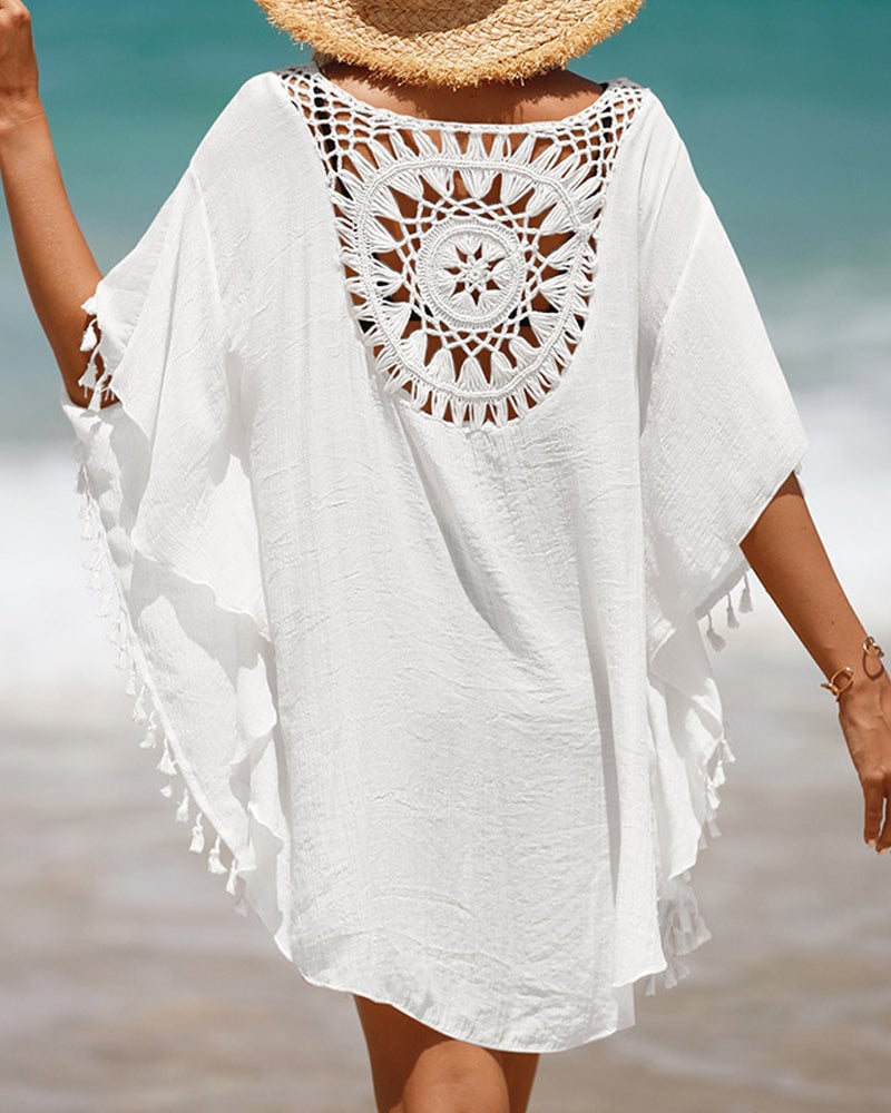 Woman wearing a white boho beach cover-up with crochet-inspired pattern and tassel hem at the beach