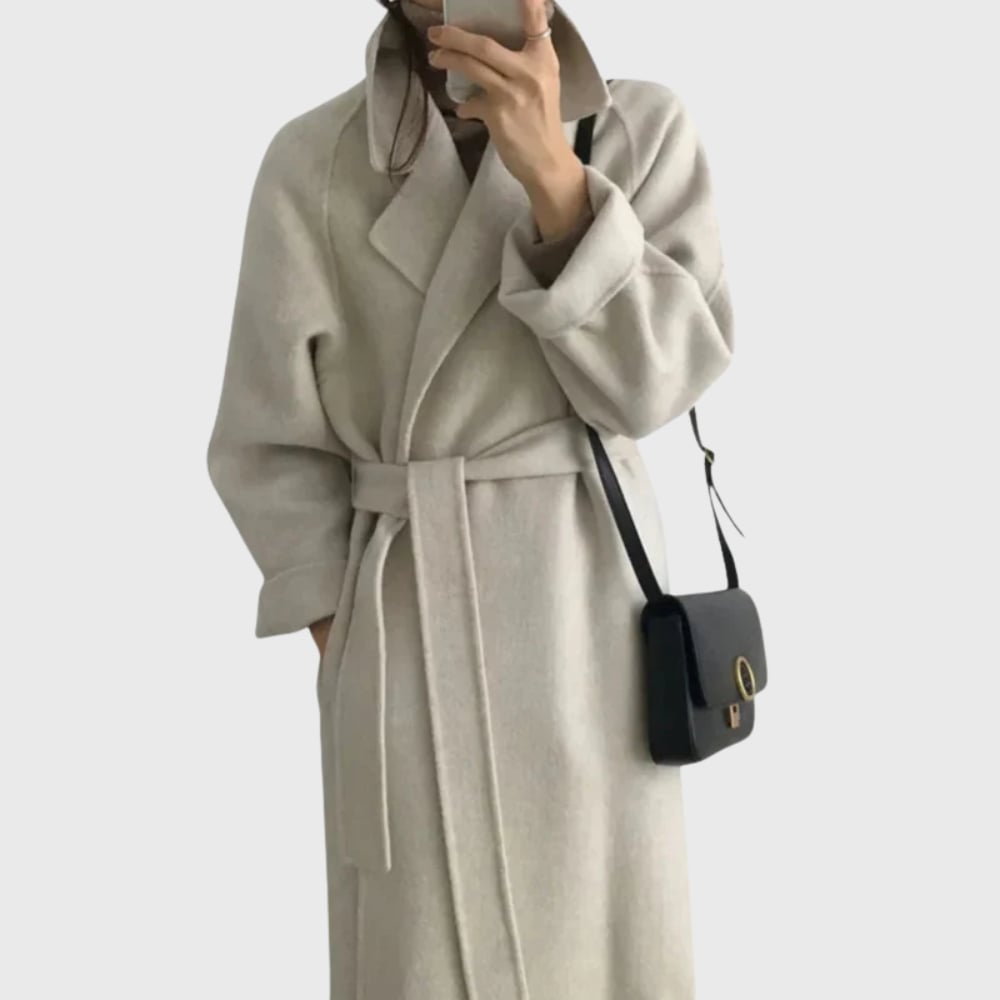Side profile of a woman in an off white belted overcoat highlighting the elegant silhouette
