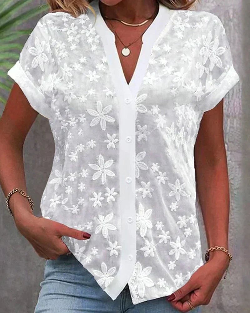 Woman wearing a white short sleeve floral lace button-down blouse with a V-neckline, cuffed sleeves, and a relaxed straight hem
