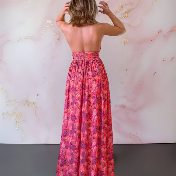 Back view of a woman in a red and pink floral maxi dress showing the open-back detail