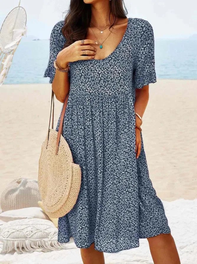 Woman wearing a navy blue ditsy floral smocked V-neck dress with flutter sleeves and a tiered flowy hem