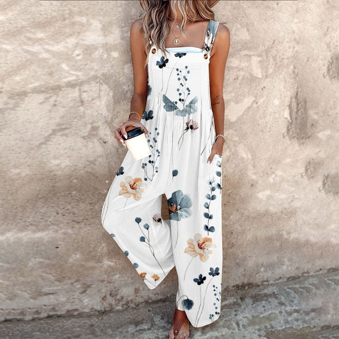 Woman wearing a white wide-leg floral overalls jumpsuit with a bold daisy print and adjustable button straps