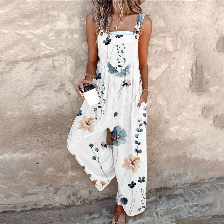 Woman wearing a white wide-leg floral overalls jumpsuit with a bold daisy print and adjustable button straps