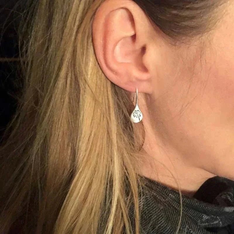 Flat lay of silver dandelion earrings alongside complementary minimalist jewelry