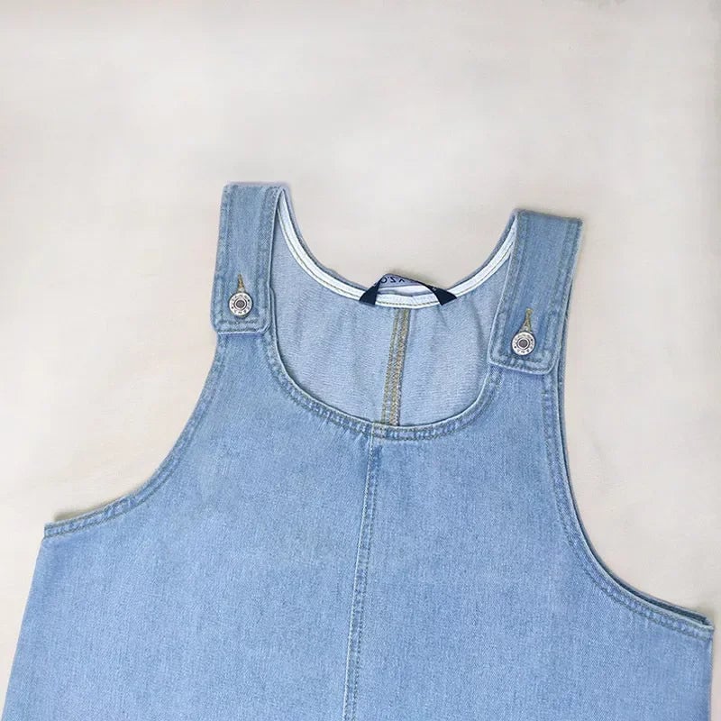 Full-length shot of the Dolores blue denim dress worn with sandals on a sunny day