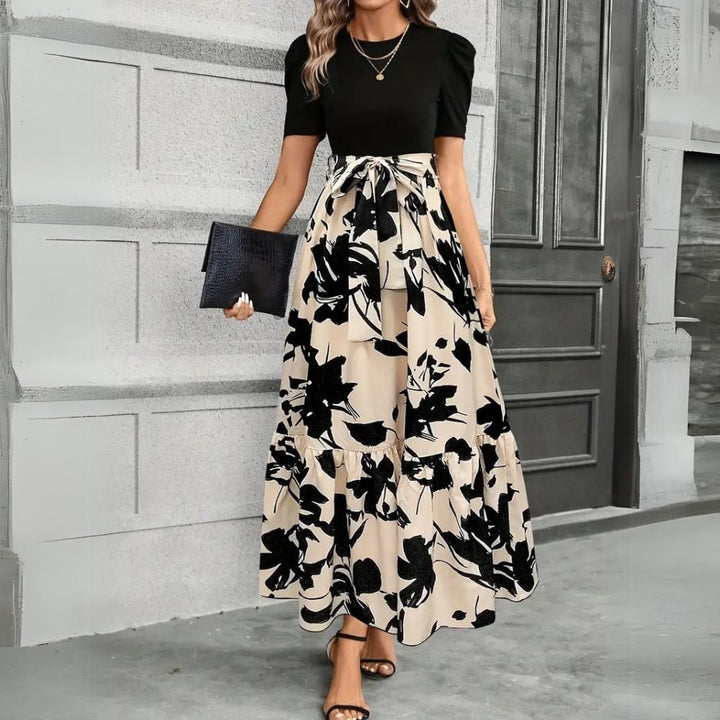 Woman wearing the Elise floral maxi dress in Floral Beige Black with puff sleeves and a self-tie bow waist, front view
