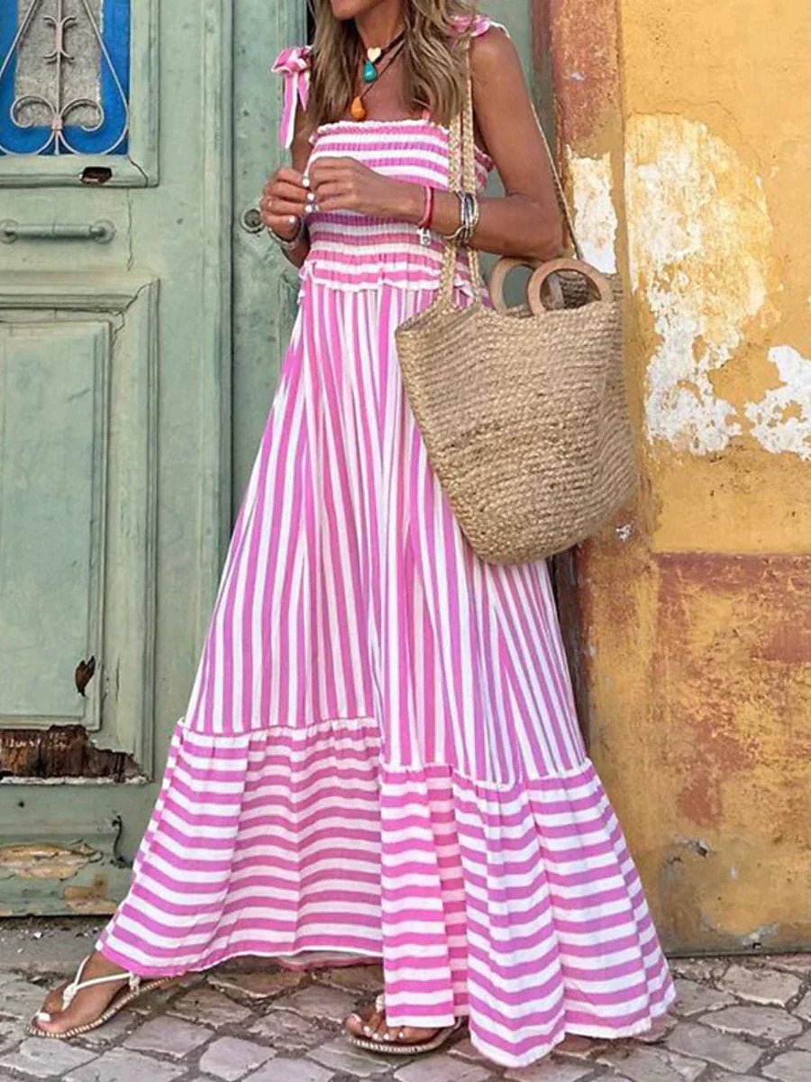 Woman wearing the Emilia elegant striped summer dress in blue with a flowy skirt and ruffled hem, styled for a summer day