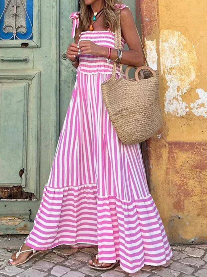 Woman wearing the Emilia elegant striped summer dress in blue with a flowy skirt and ruffled hem, styled for a summer day