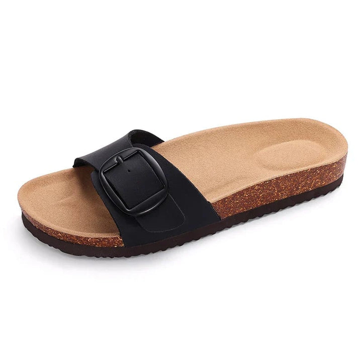 Flora flat sandals in black worn on feet, standing on light pavement
