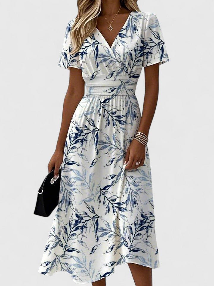 Woman wearing a white floral wrap midi dress with navy botanical leaf print, V-neckline, flutter sleeves, and ruched elasticated waist