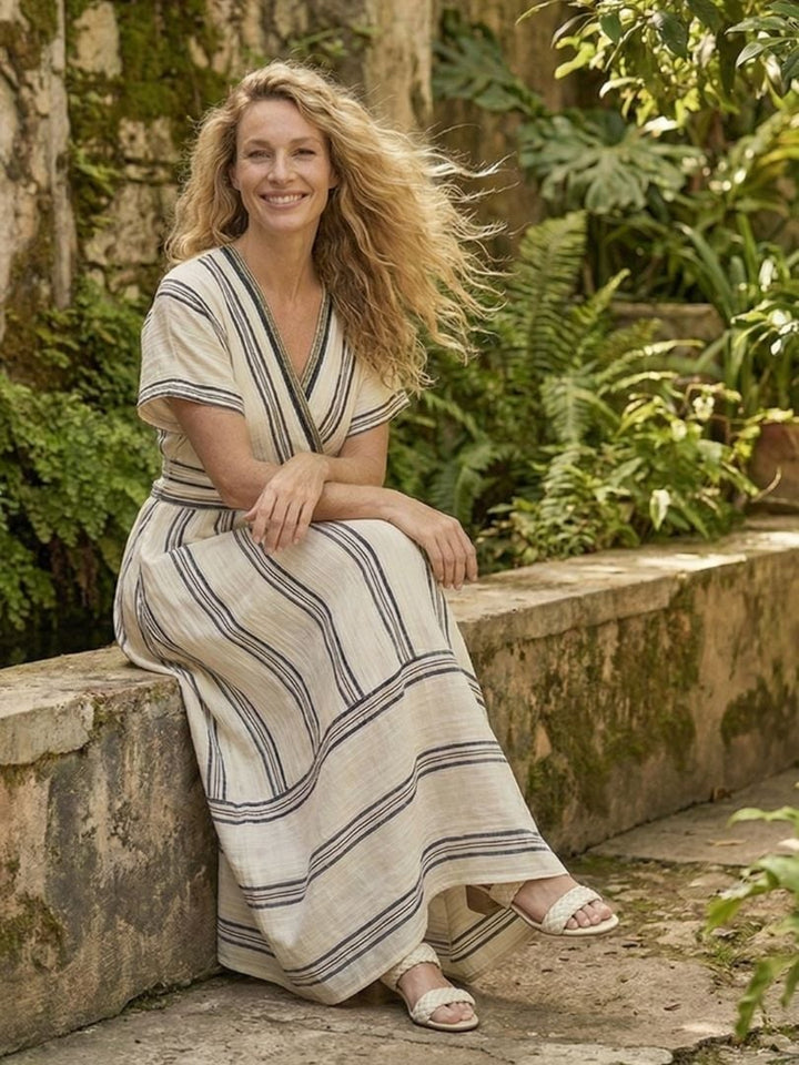Full-length lifestyle shot of a woman in a white striped V-neck wrap midi dress outdoors