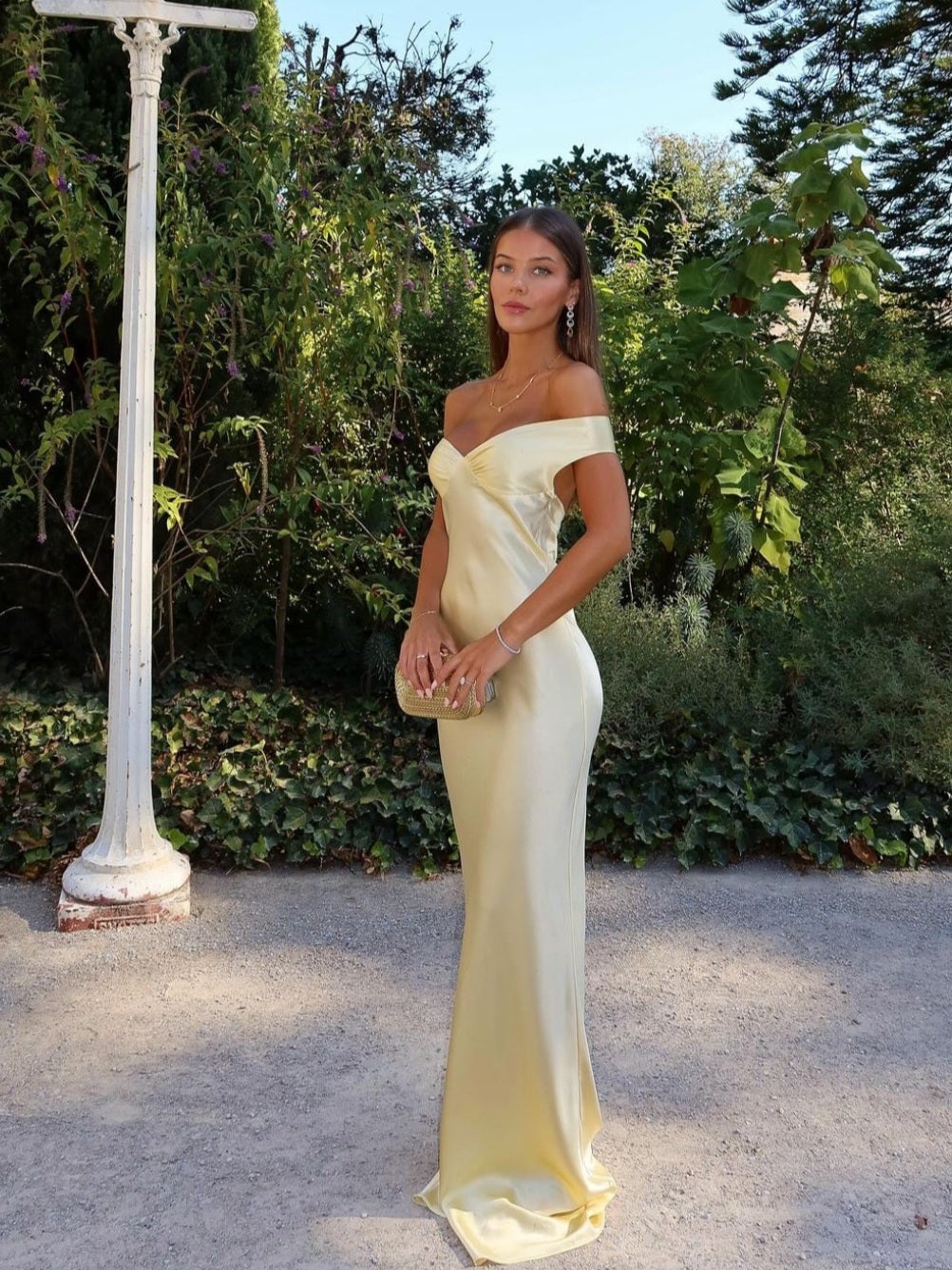 Woman wearing a gold off-shoulder satin evening gown with a sculpted bodice and flowing skirt