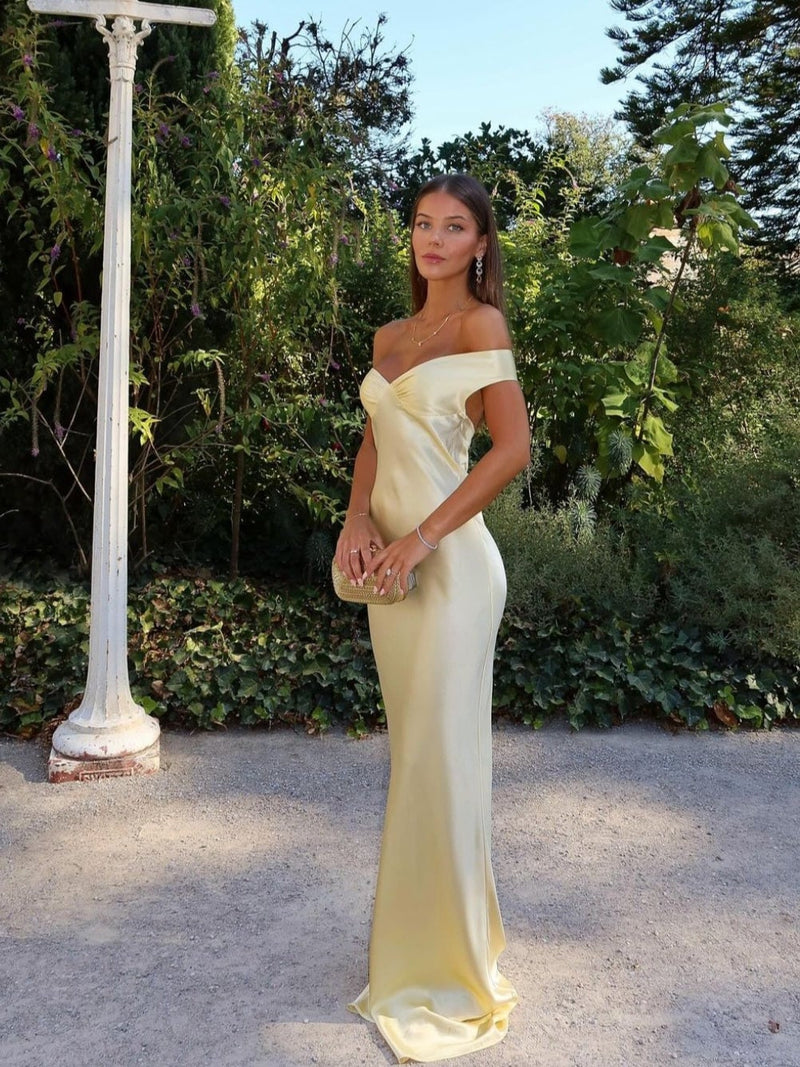 Woman wearing a gold off-shoulder satin evening gown with a sculpted bodice and flowing skirt