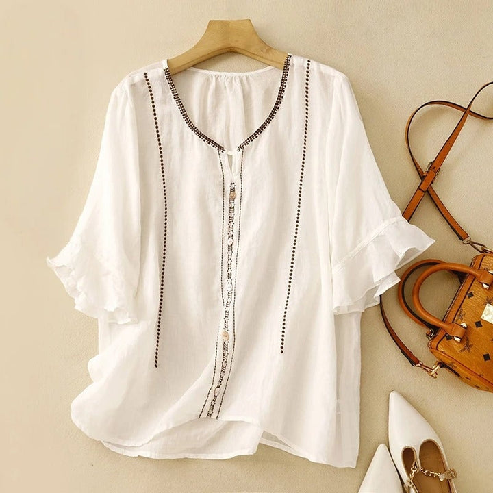 Front view of a white ruffle sleeve blouse with delicate embroidery and pearl-style button front on a female model