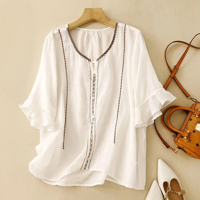 Front view of a white ruffle sleeve blouse with delicate embroidery and pearl-style button front on a female model