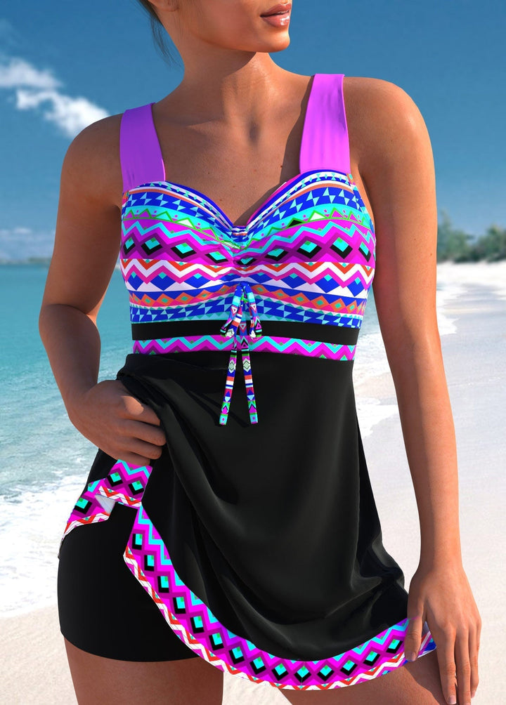 Woman wearing a bold geometric patterned swim dress with ruched bust and built-in shorts, standing poolside