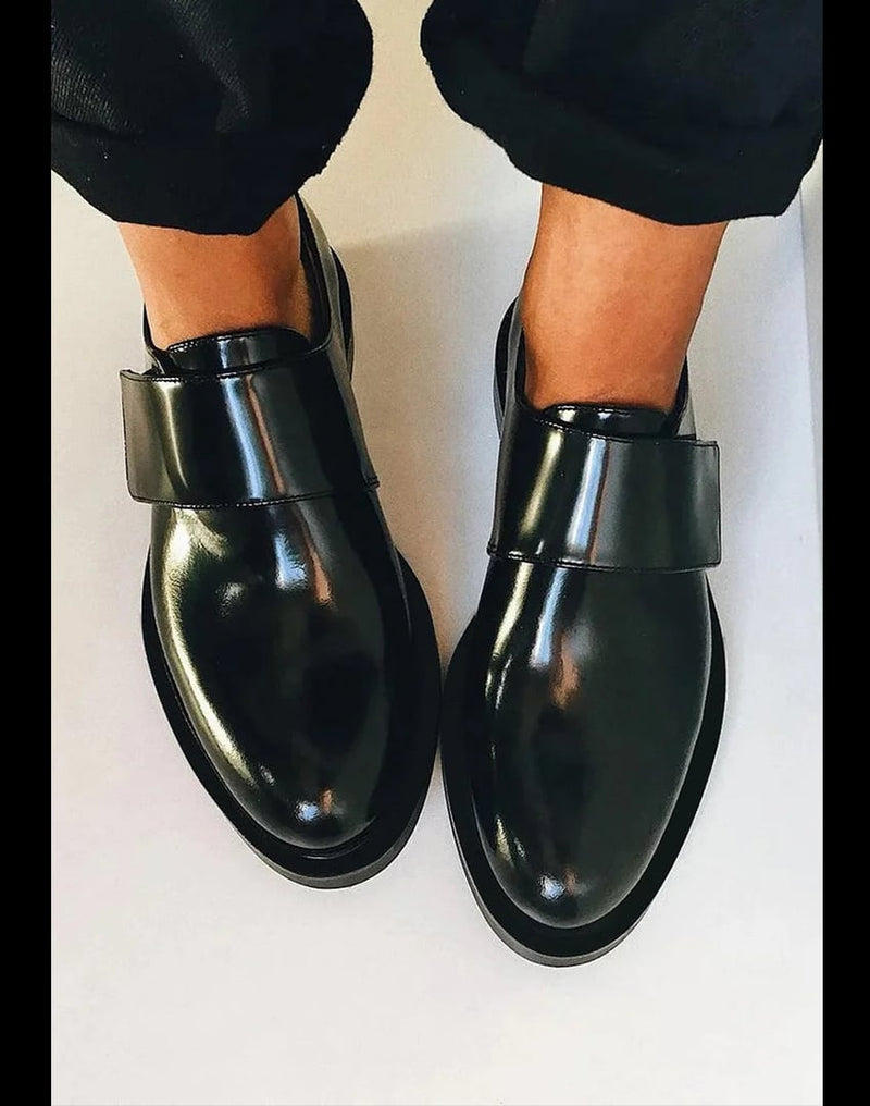 Black Harleigh strap loafers shown from a front three-quarter angle highlighting the minimalist strap detail and sleek silhouette