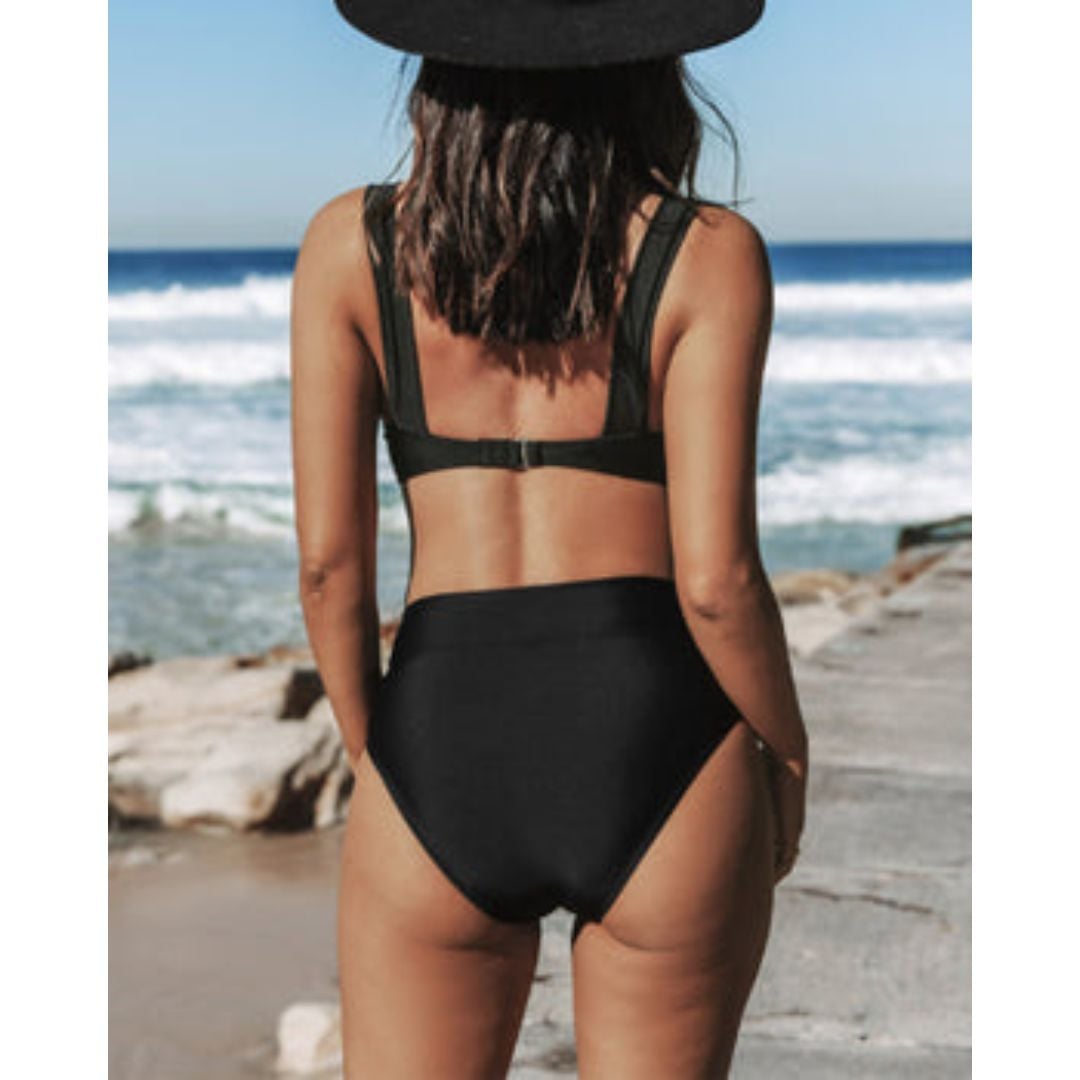 Woman in a solid black one-piece swimsuit walking on a sandy beach