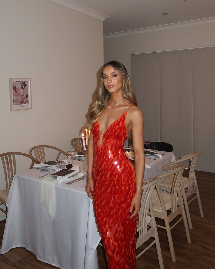 Woman in red sequin backless dress posing at a styled event setting, three-quarter view