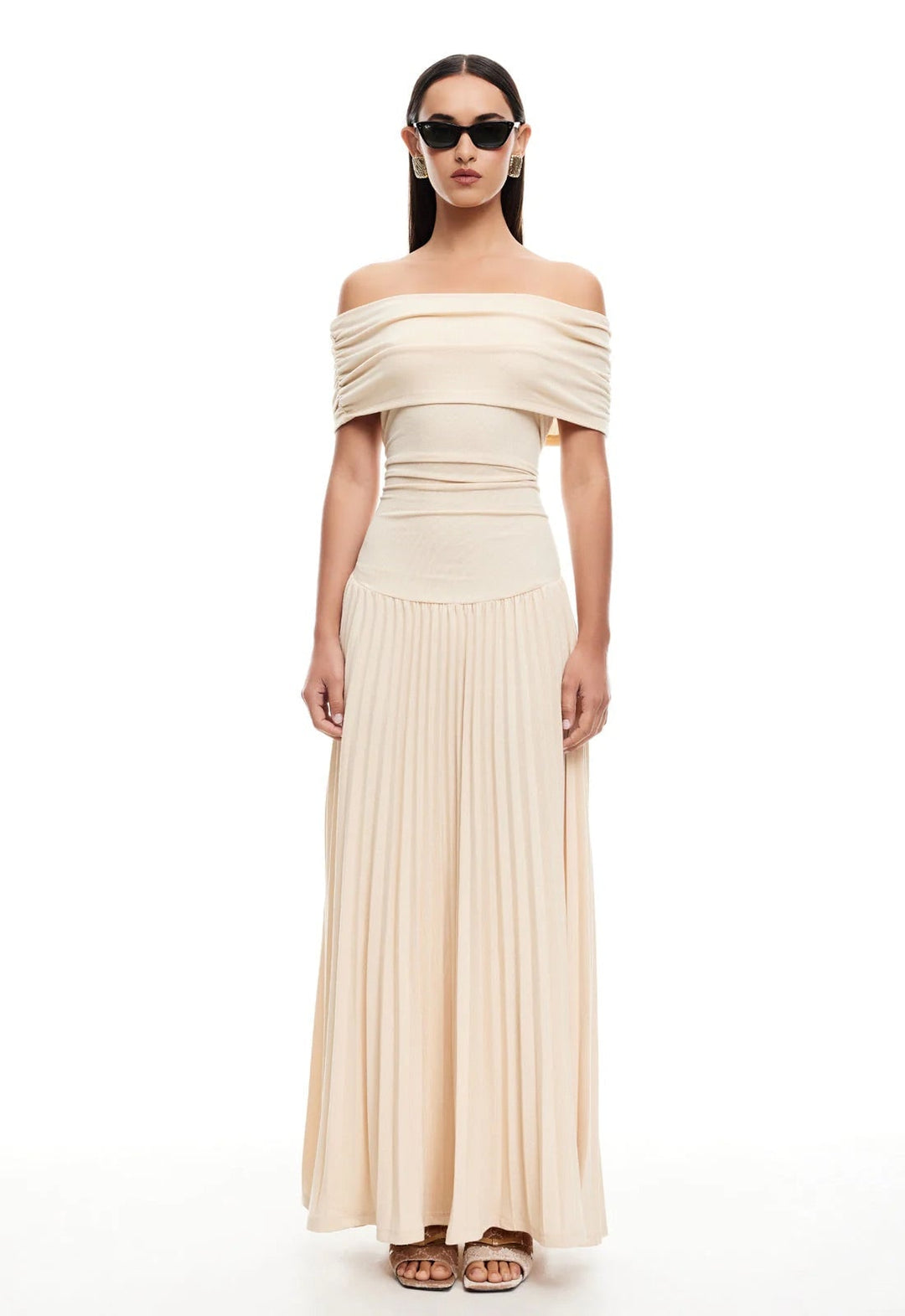 Front view of a woman in a cream maxi dress walking on a sunny beach, dress flowing in the breeze