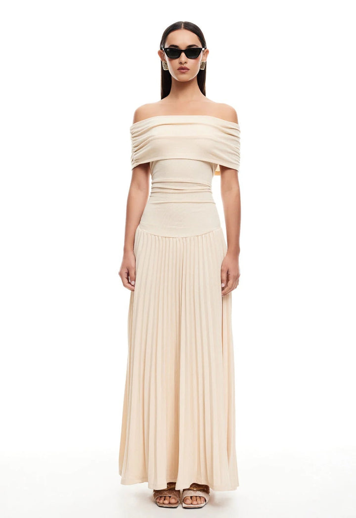 Front view of a woman in a cream maxi dress walking on a sunny beach, dress flowing in the breeze