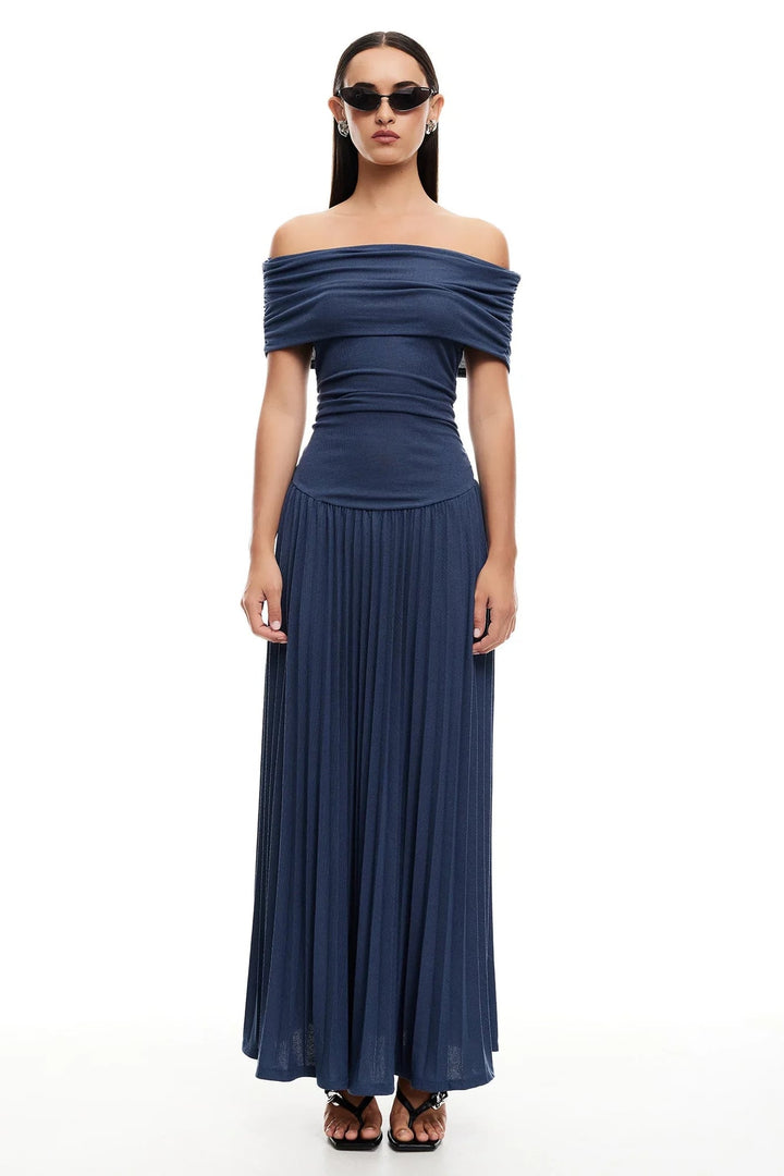 Woman in a navy flowy maxi dress standing against a white wall, clean and minimal styling for everyday wear